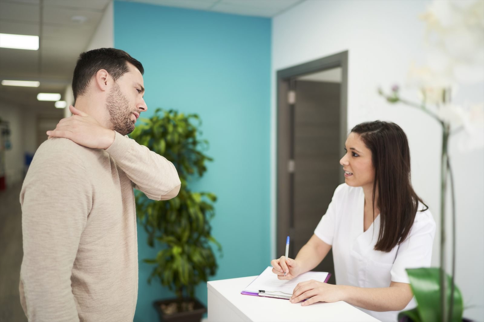 A clinic staff member speaking with a visitor at a reception desk.